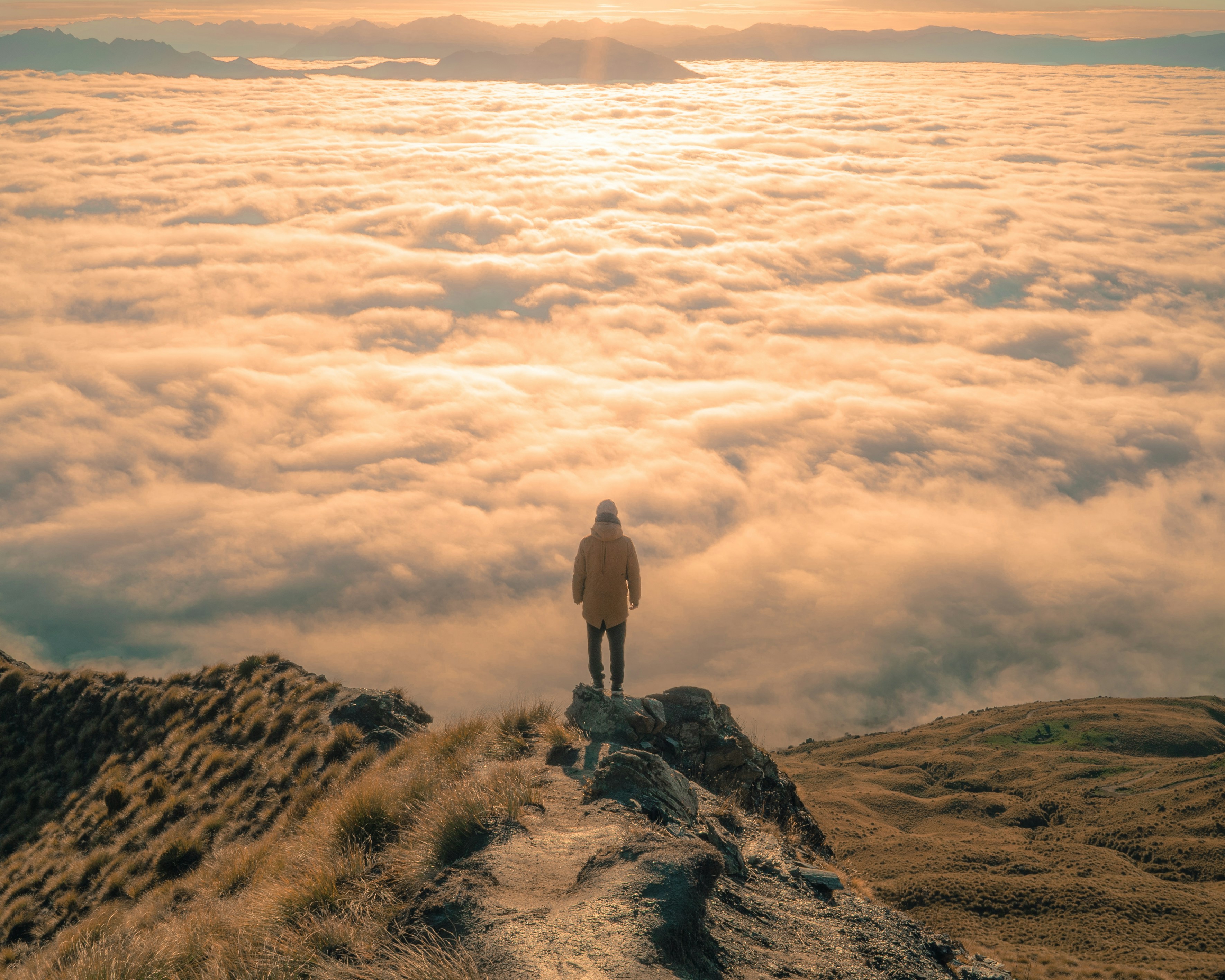A lone figure on a mountainside above a golden sea of clouds at sunrise